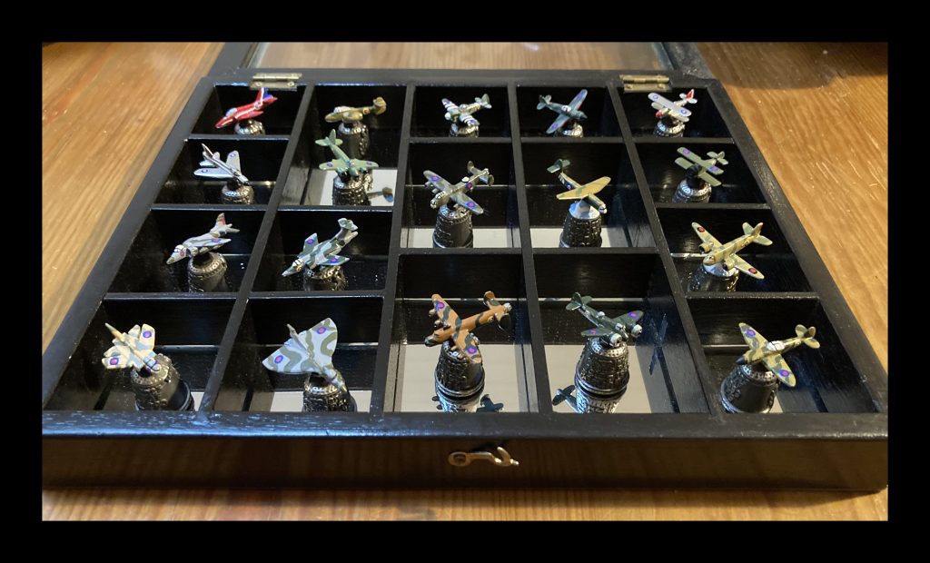 Picture of a display case with 18 model aeroplanes mounted on metal thimbles.