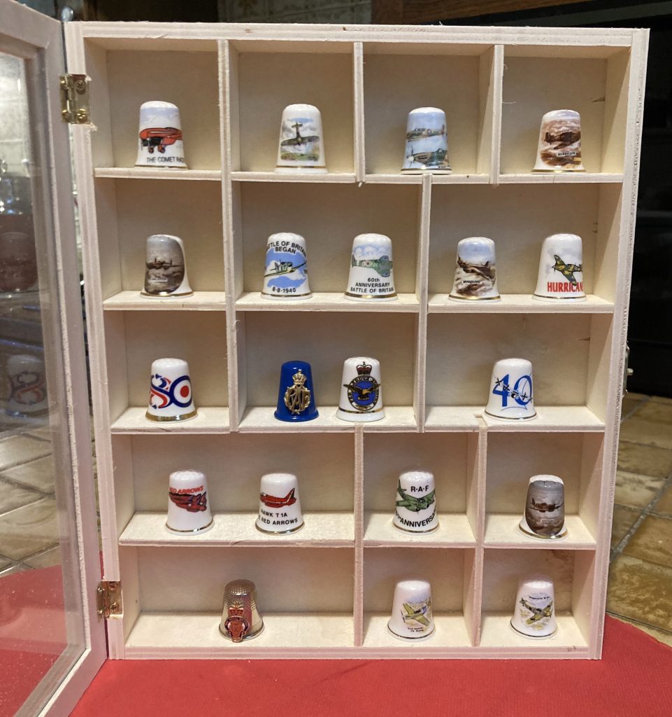 Picture of a display case with 20 decorated ceramic thimbles with an aviation theme